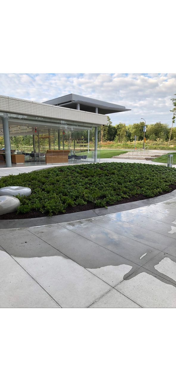 Modern outdoor pavilion with glass walls, greenery, and paved walkway under a cloudy sky