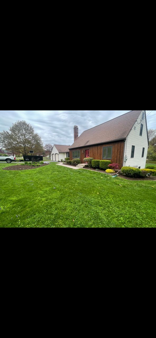 Rural farmhouse with red barn, white house, and green lawn under a cloudy sky