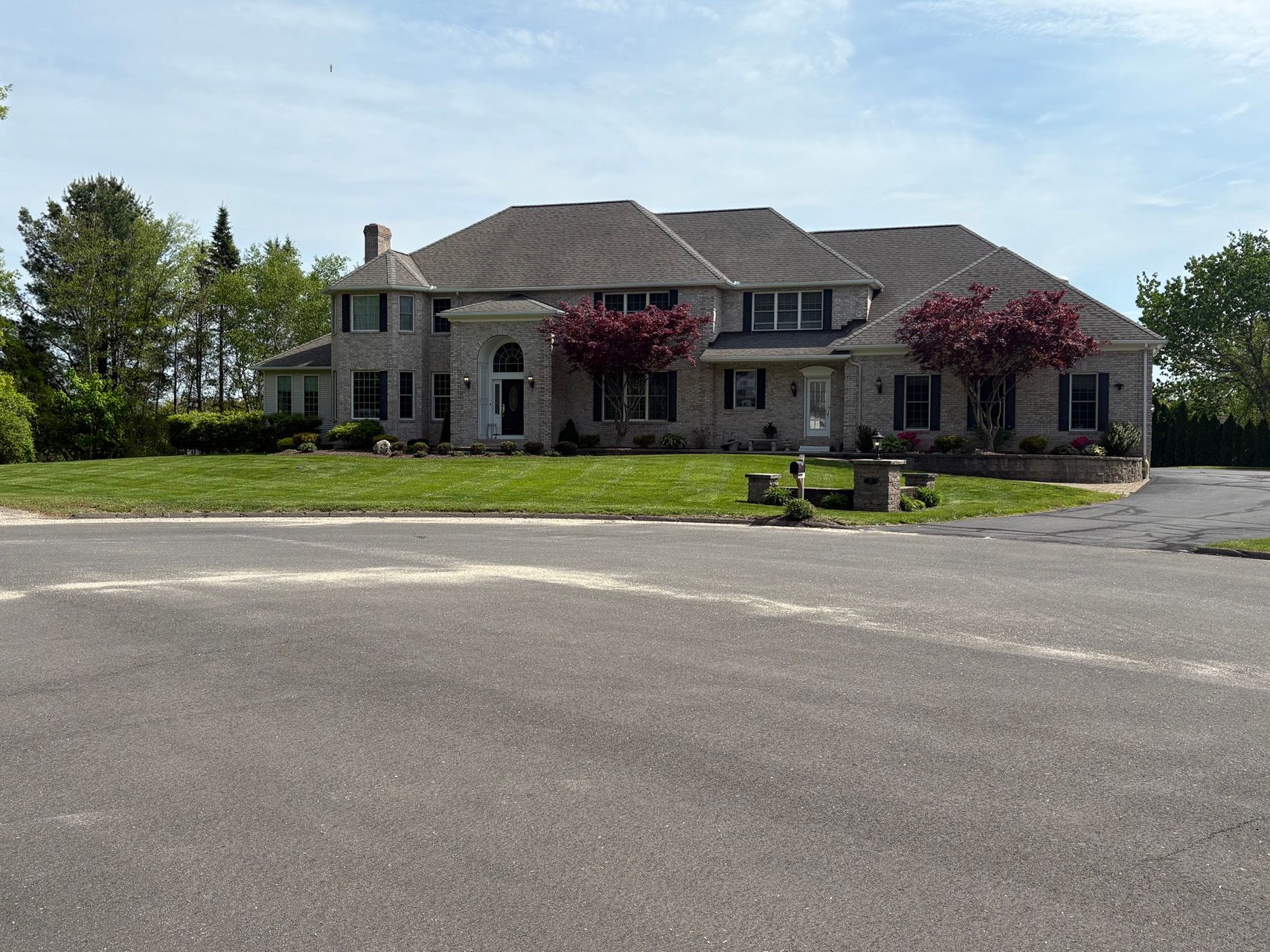 Large stone house with red trees and a wide asphalt driveway in front