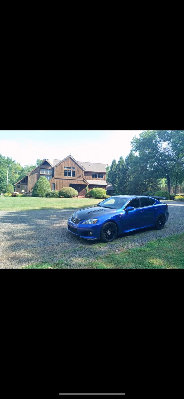 Blue car parked on a grassy driveway in front of a large house with trees around it