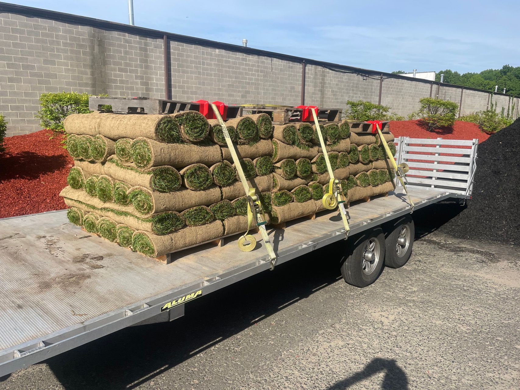 Landscaped turf rolls strapped on a flatbed trailer in a sunny parking lot.