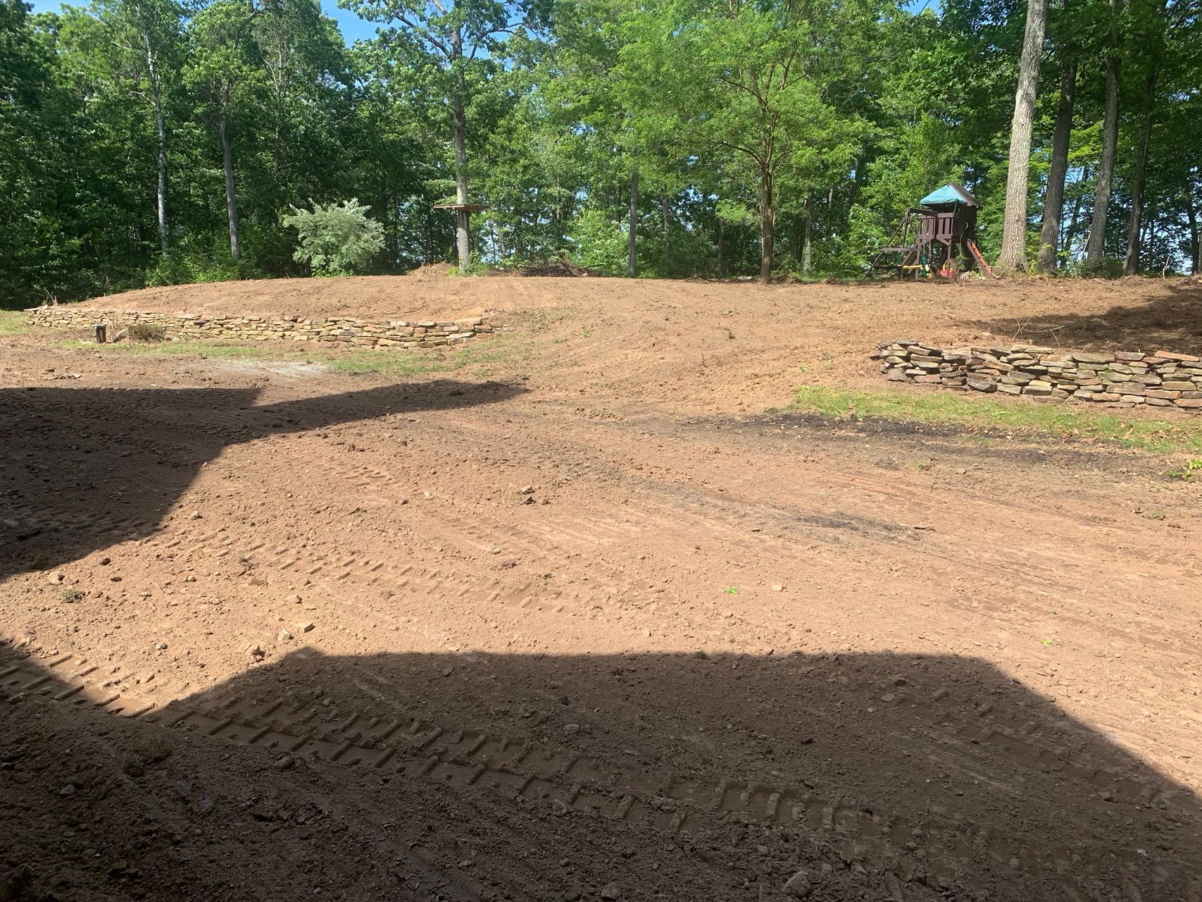 Dirt mound under trees in a park, with a small playground structure in the background.