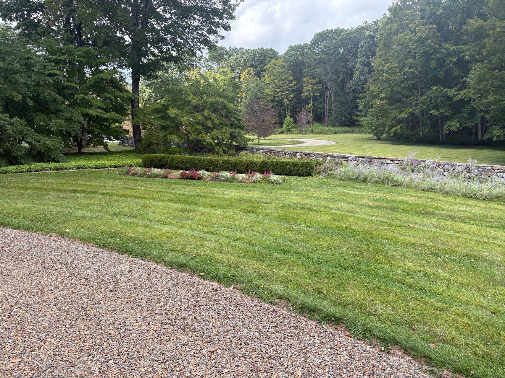 Gravel path beside a green lawn, flower bed, and trees in a park-like landscape.