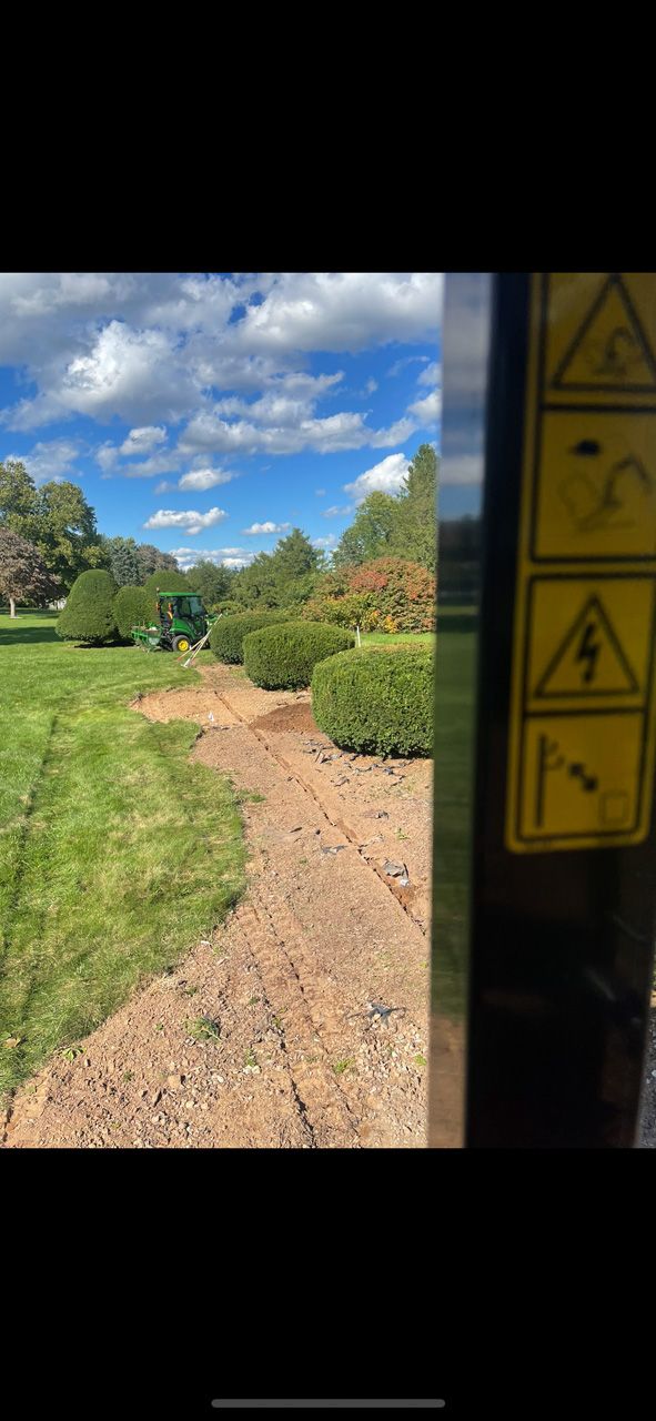 Gravel path through a green garden under a blue sky, viewed past a doorway with caution stickers.