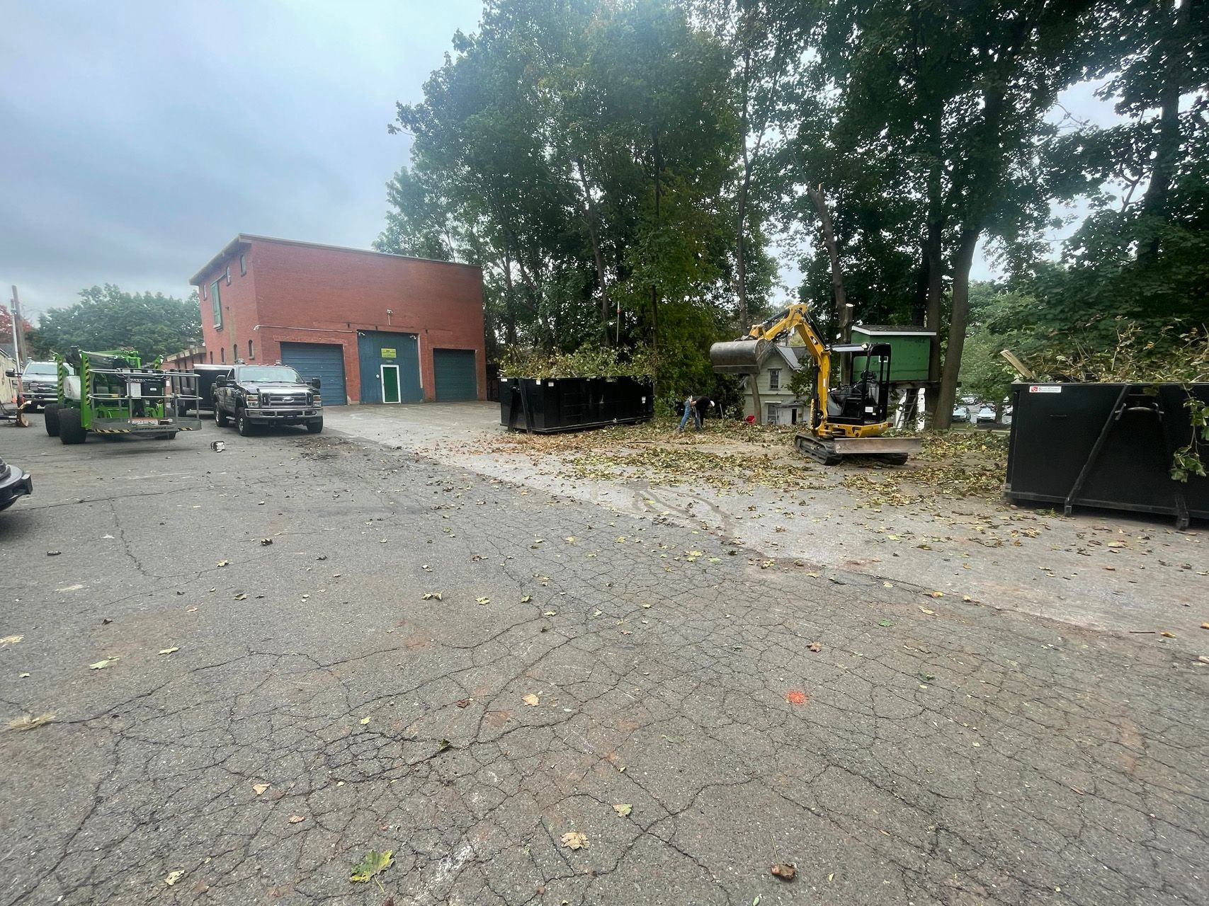 Construction site with excavator, trucks, and red building on a wet paved lot