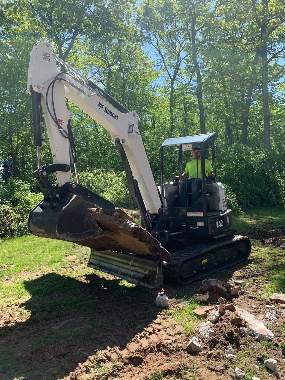 White excavator digging soil in a wooded area on a sunny day
