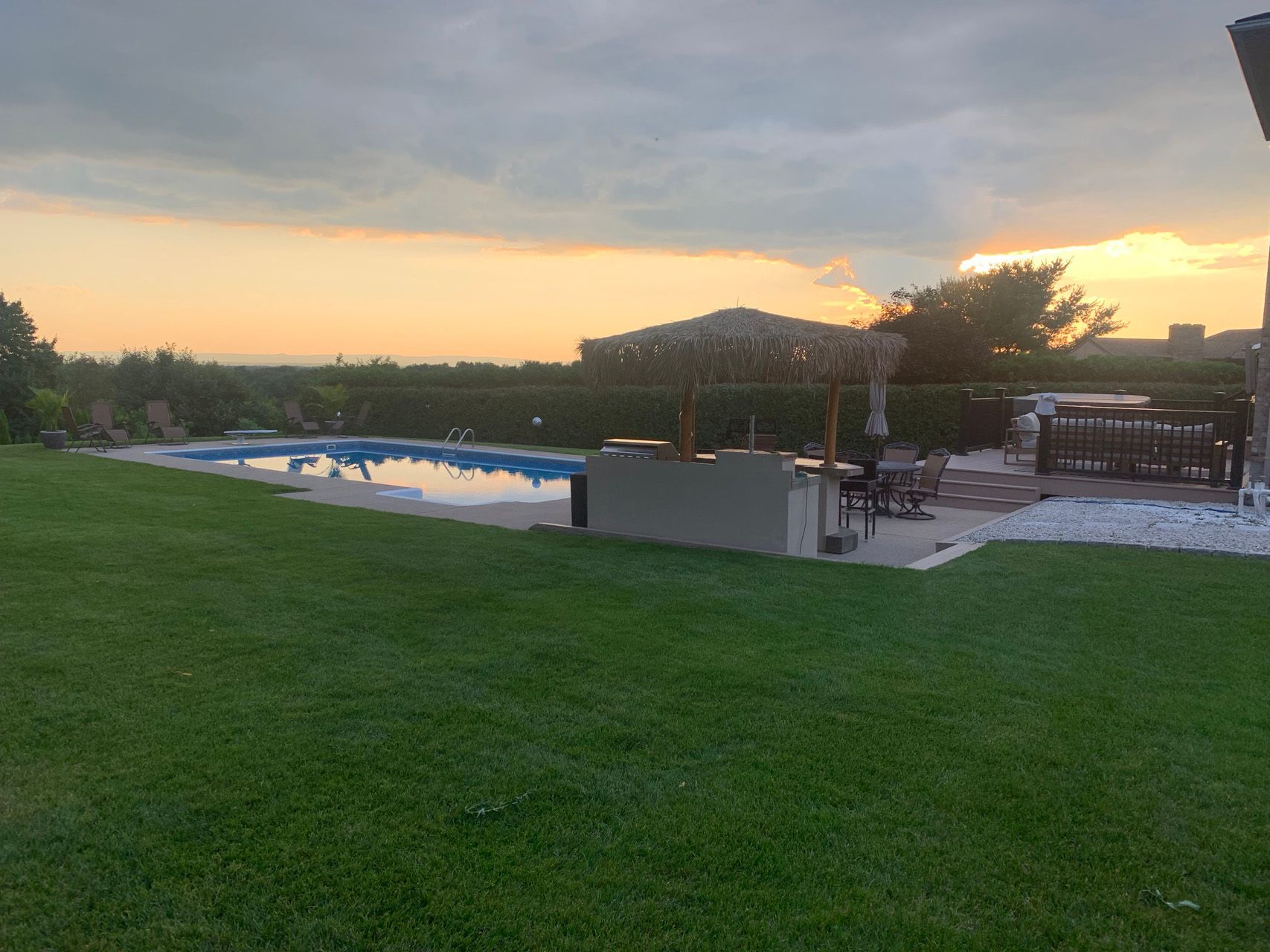 Grassy yard at sunset with a swimming pool and covered patio seating area