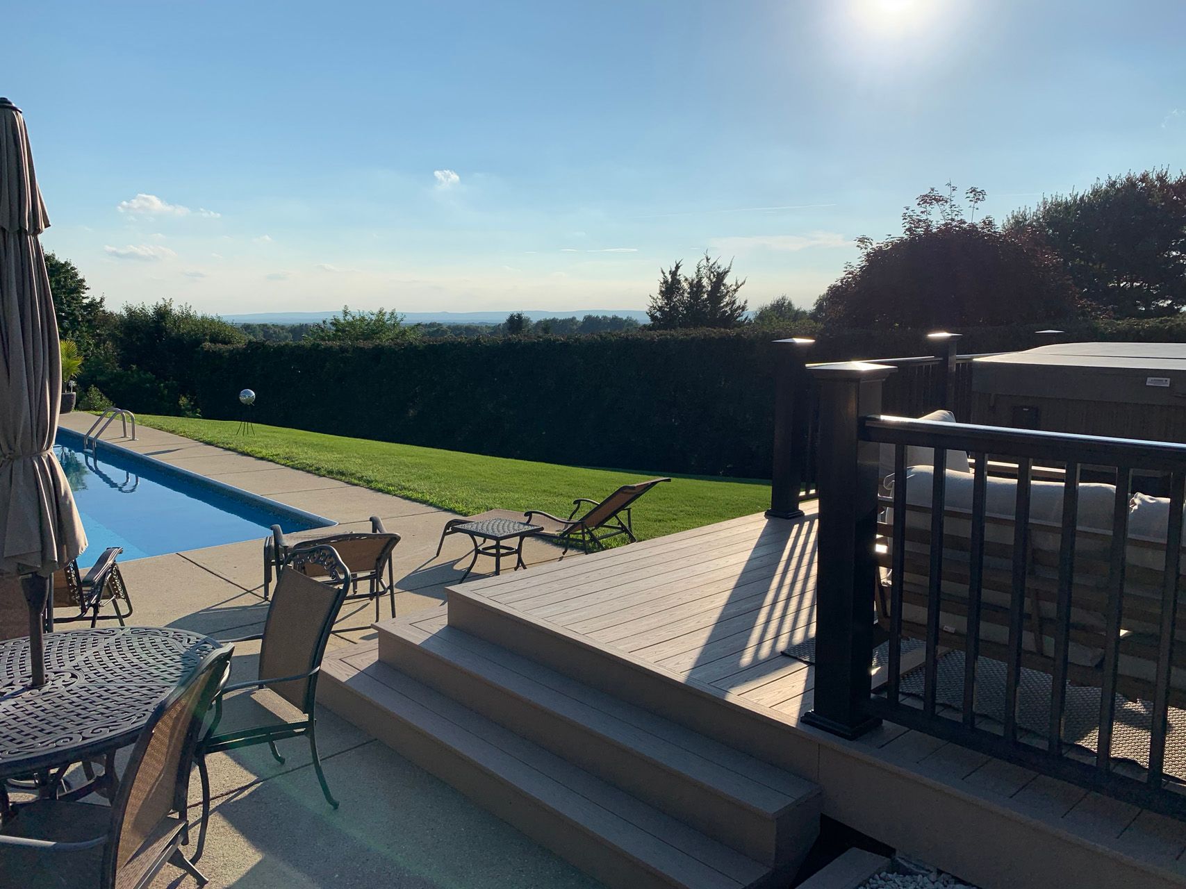 Backyard patio with pool, lounge chairs, steps, and bright sun over a grassy lawn