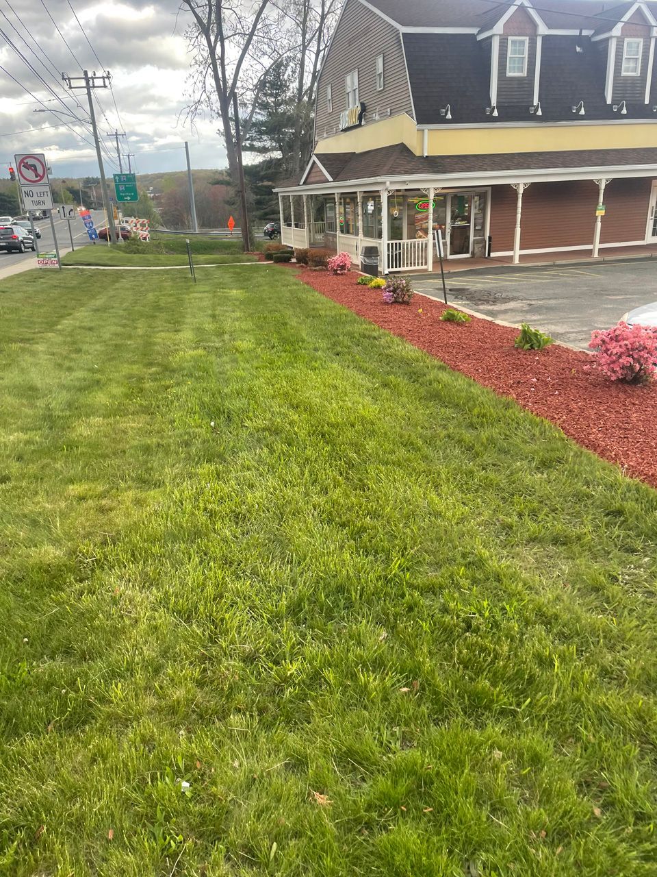 Suburban house with a porch beside a grassy lawn and red mulch landscaping by a roadside