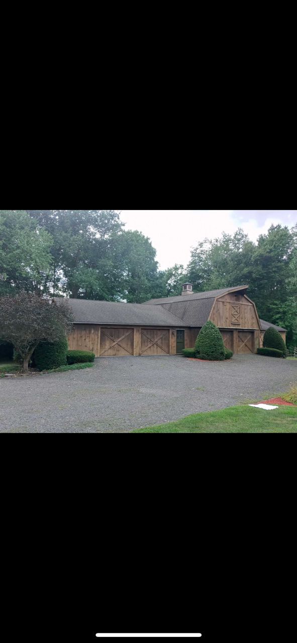 Large rustic wooden building with a gravel driveway, surrounded by trees under an overcast sky.