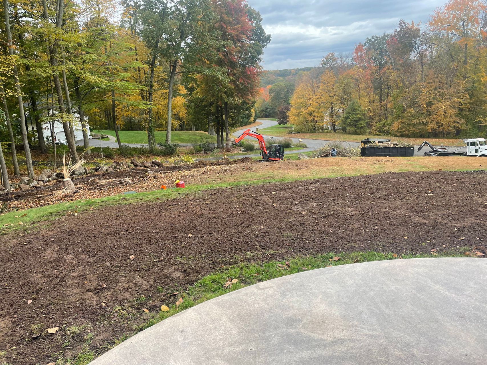 Construction work beside a newly planted lawn with excavator and autumn trees in the background