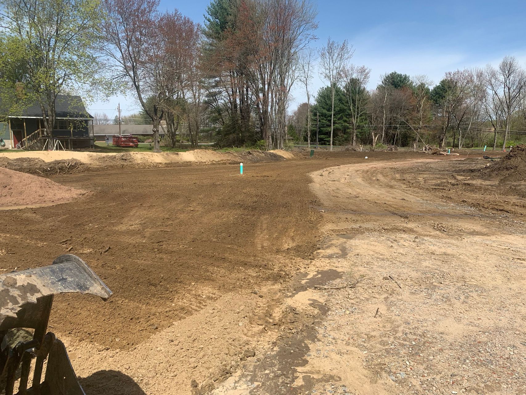 Cleared dirt lot with grading marks, trees in the background, and a small turquoise marker in the center.