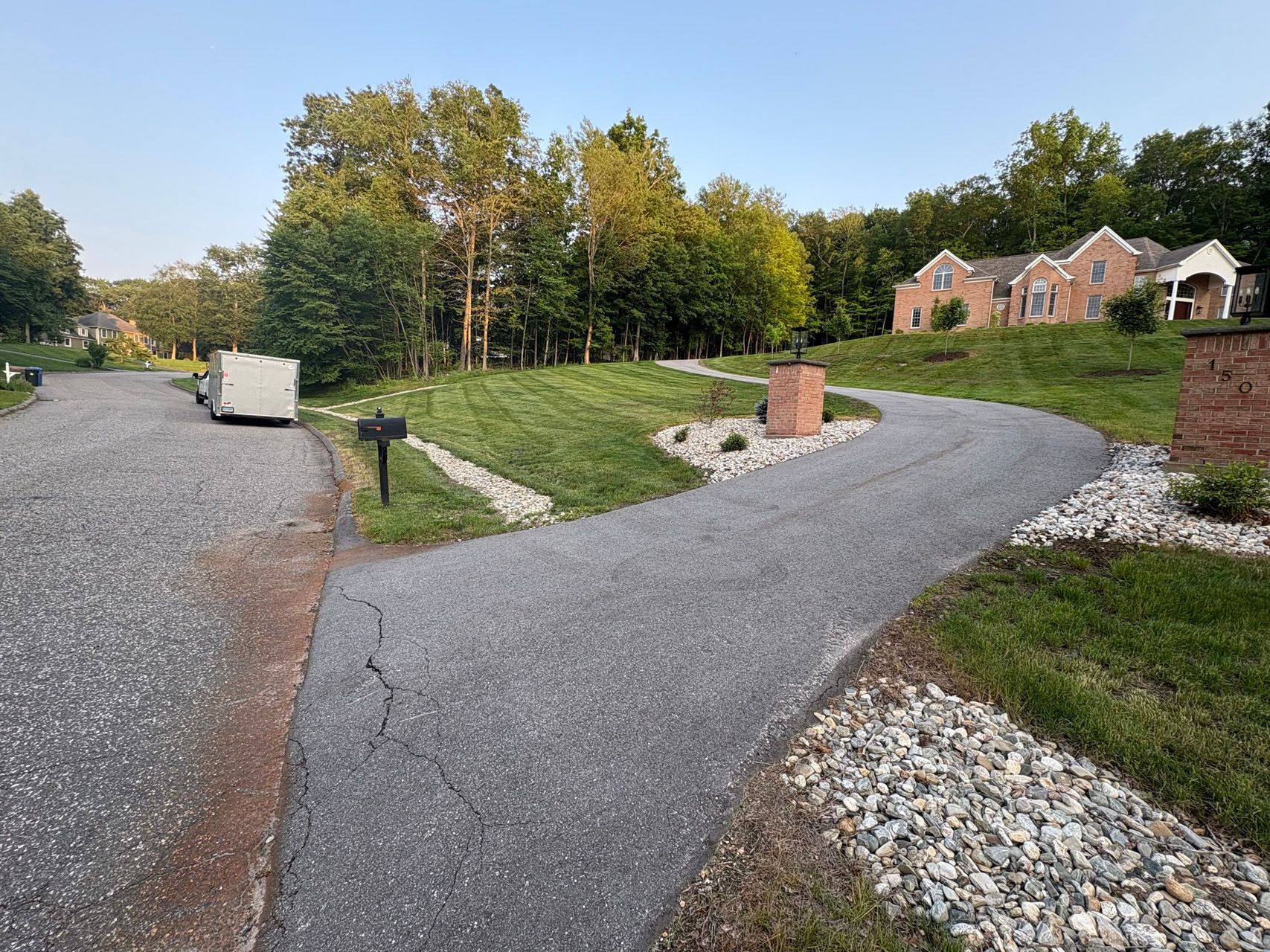 Curved gravel driveway beside a landscaped lawn and brick homes under a clear sky