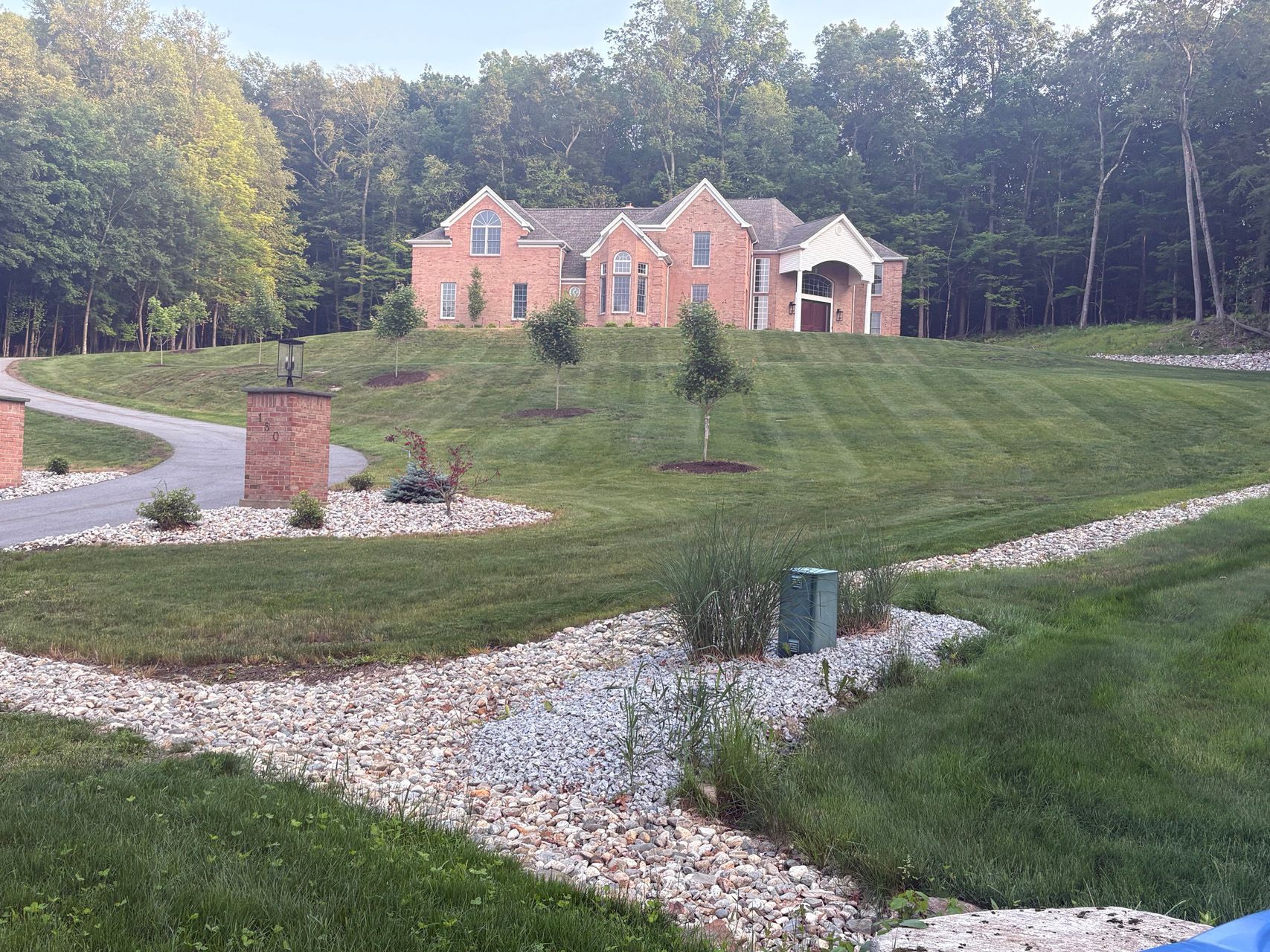 Brick house on a grassy hill with winding gravel paths and trees in the background
