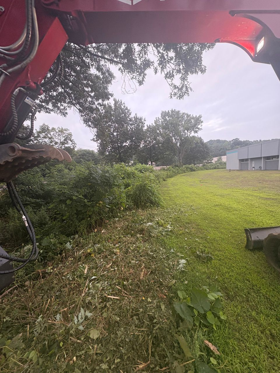 Cherry picker view of a grassy slope with trees and a building under an overcast sky