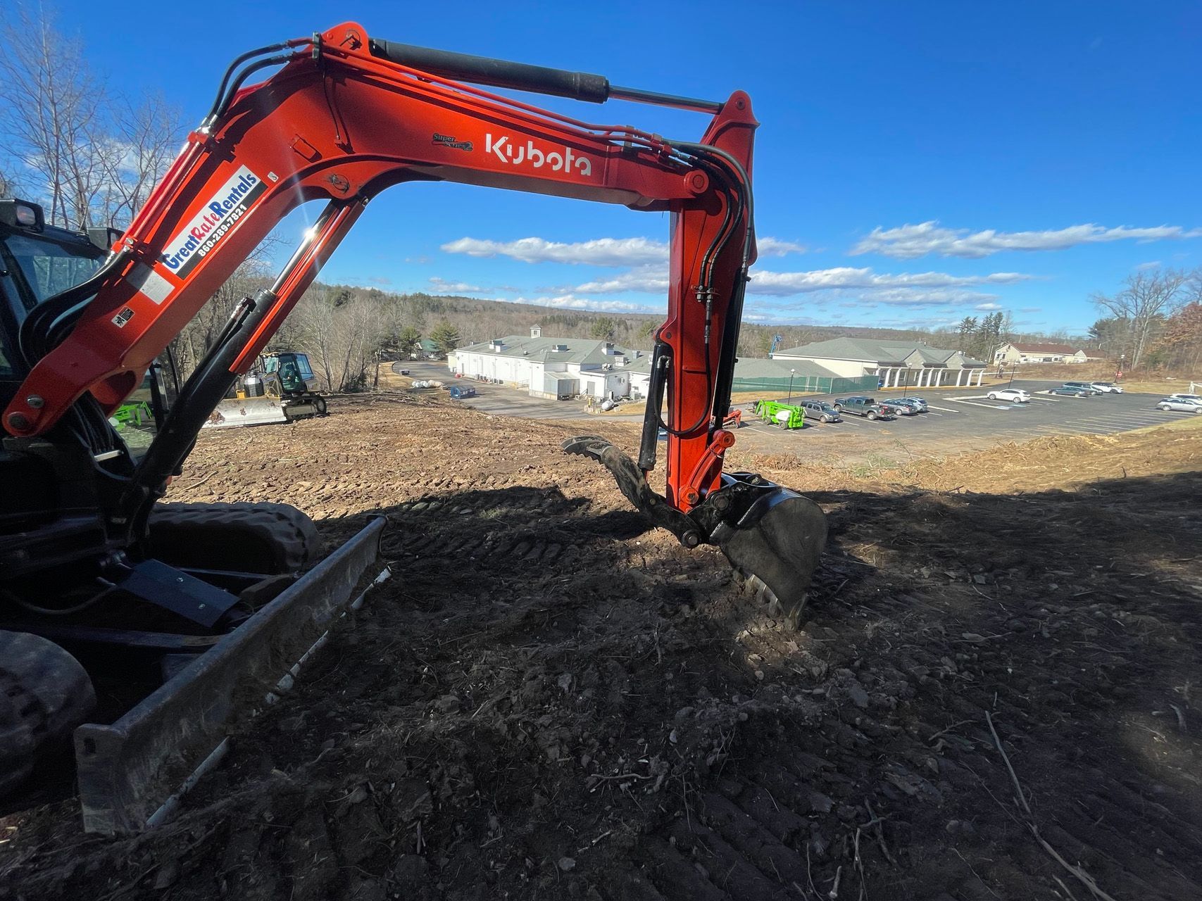 Red excavator digging dirt at a construction site under a blue sky