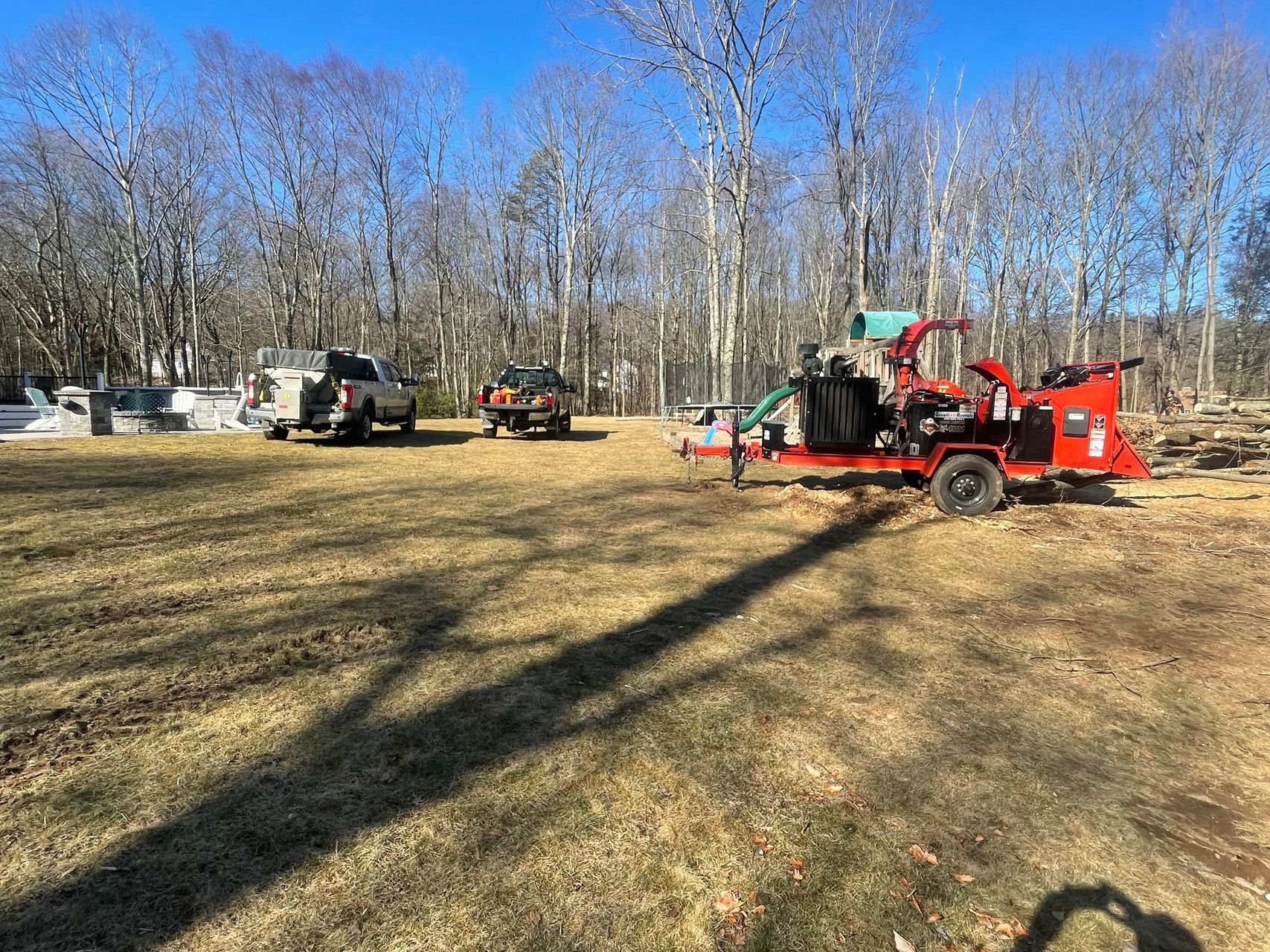 Red wood chipper beside trucks in a wooded clearing under a blue sky