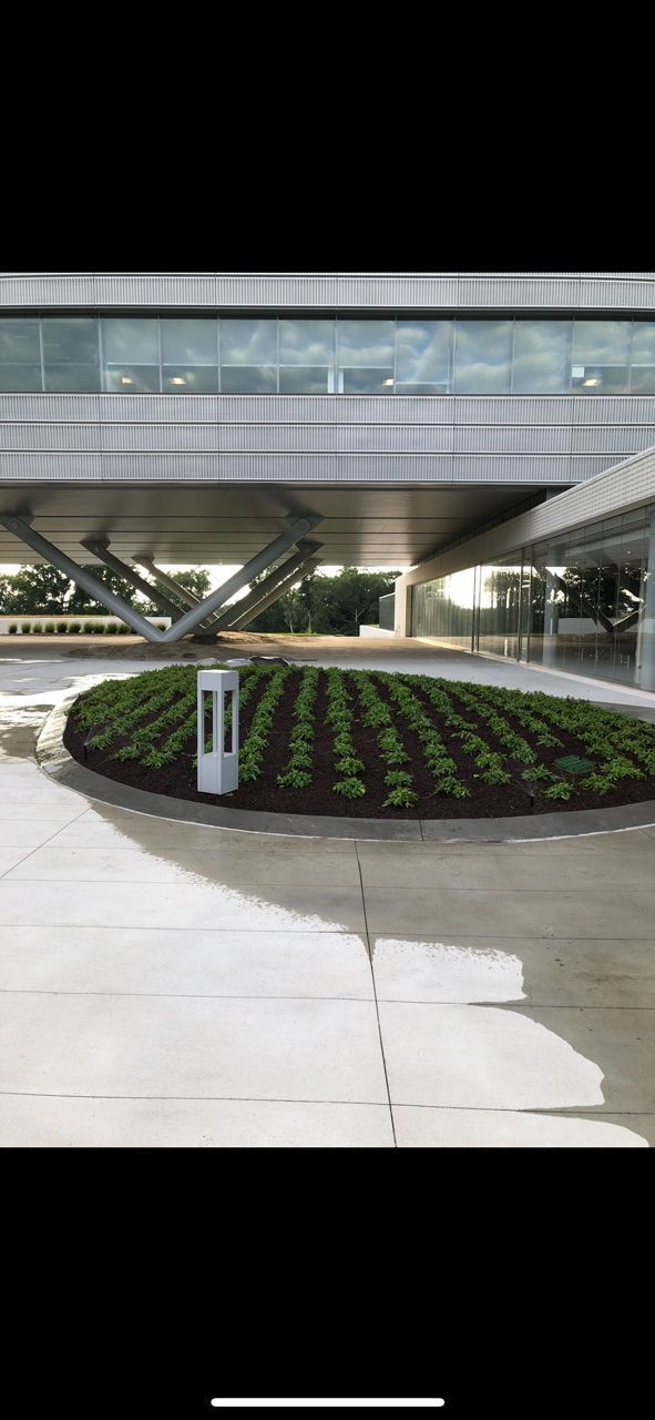 Circular flower bed under a modern building with glass railings and a covered walkway.