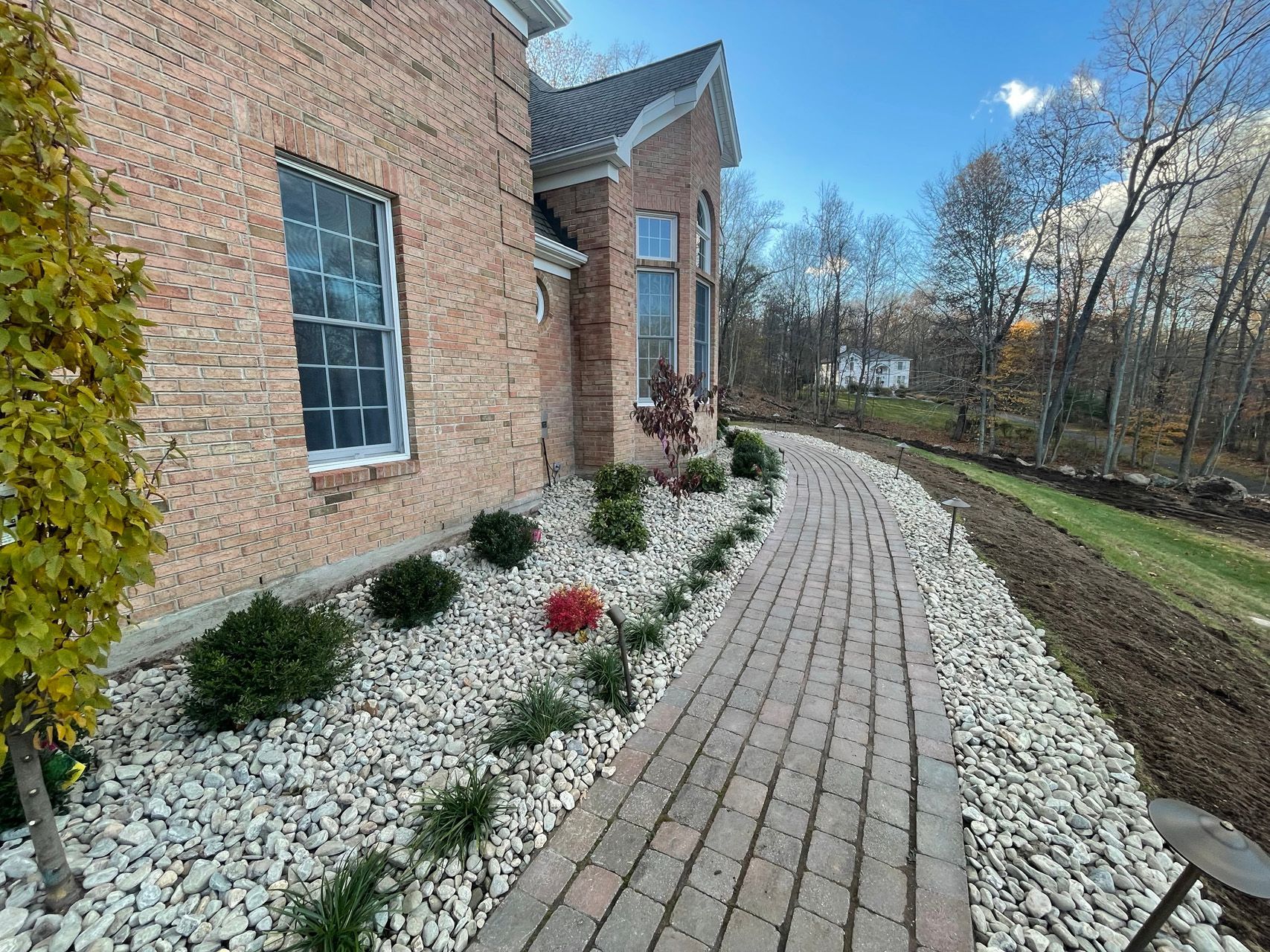 Brick house exterior with curved paver walkway and white decorative stones in a landscaped yard