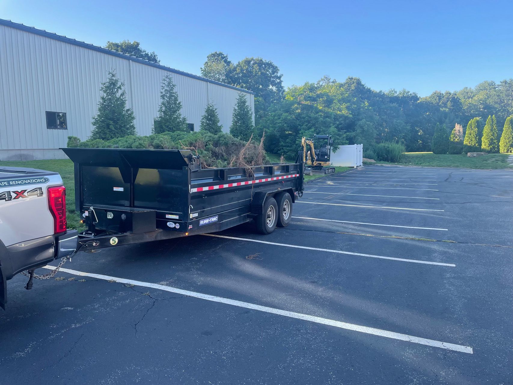 Pickup truck with flatbed trailer parked in an empty lot beside a warehouse.