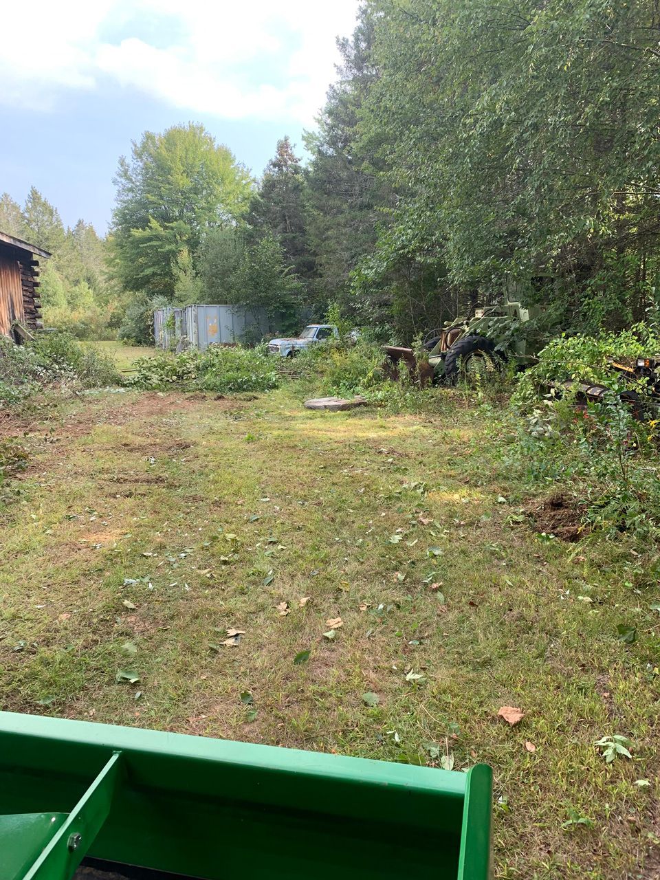 Grassy yard with trees and a green tractor bucket in the foreground