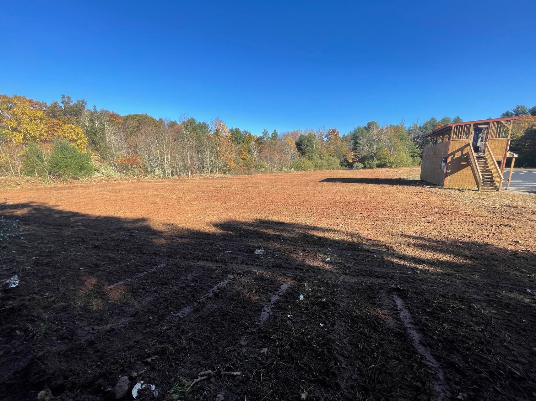 Open dirt field under blue sky with autumn trees and a tractor at right