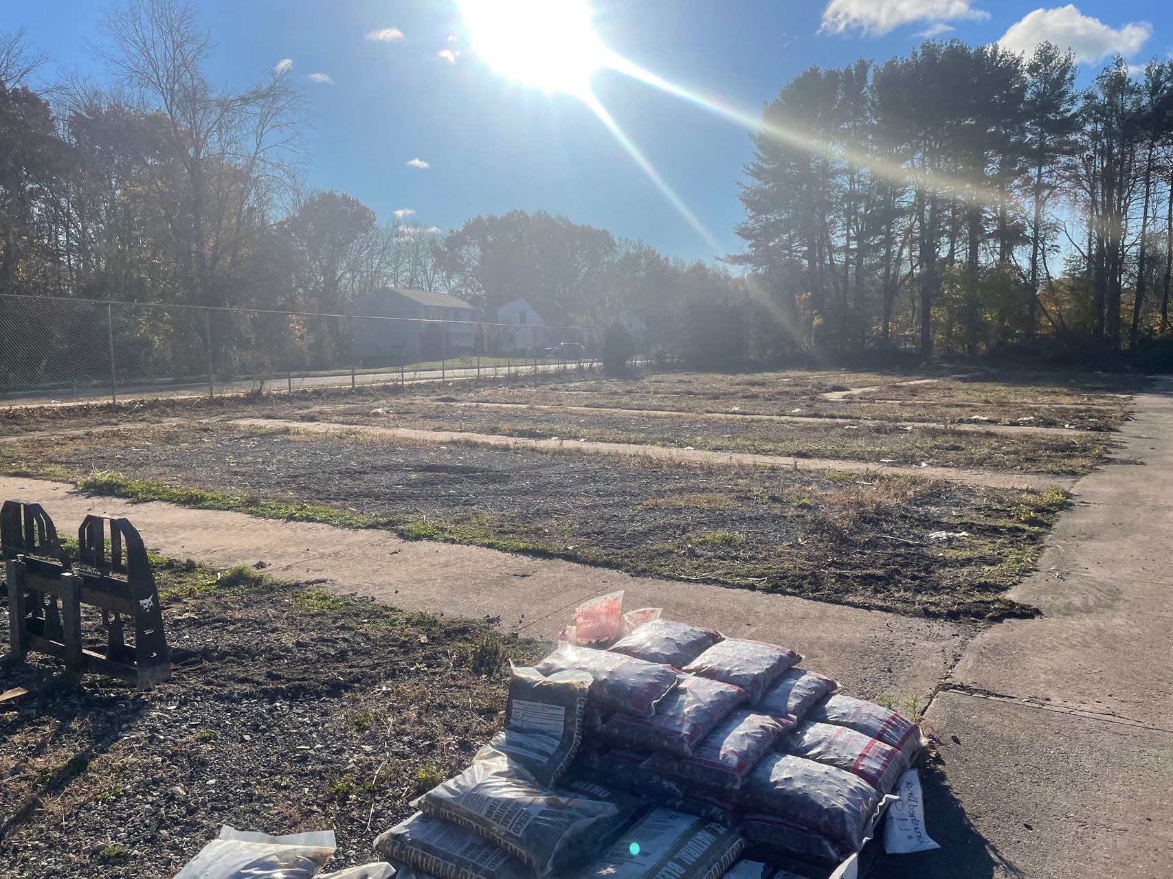 Sunlit field with rows of covered materials, a path, and stacked bags in the foreground