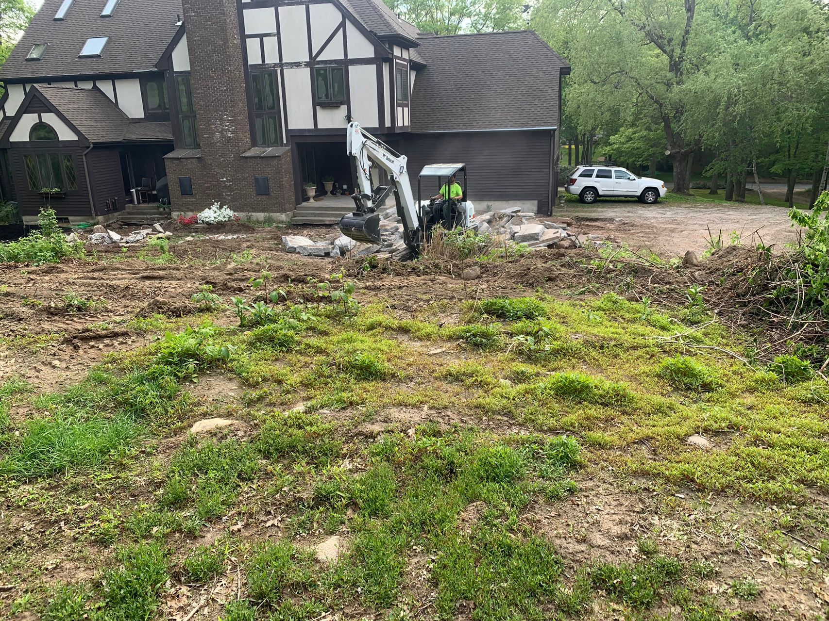 Demolished house with rubble in yard, a worker in a neon vest, and a white SUV nearby.