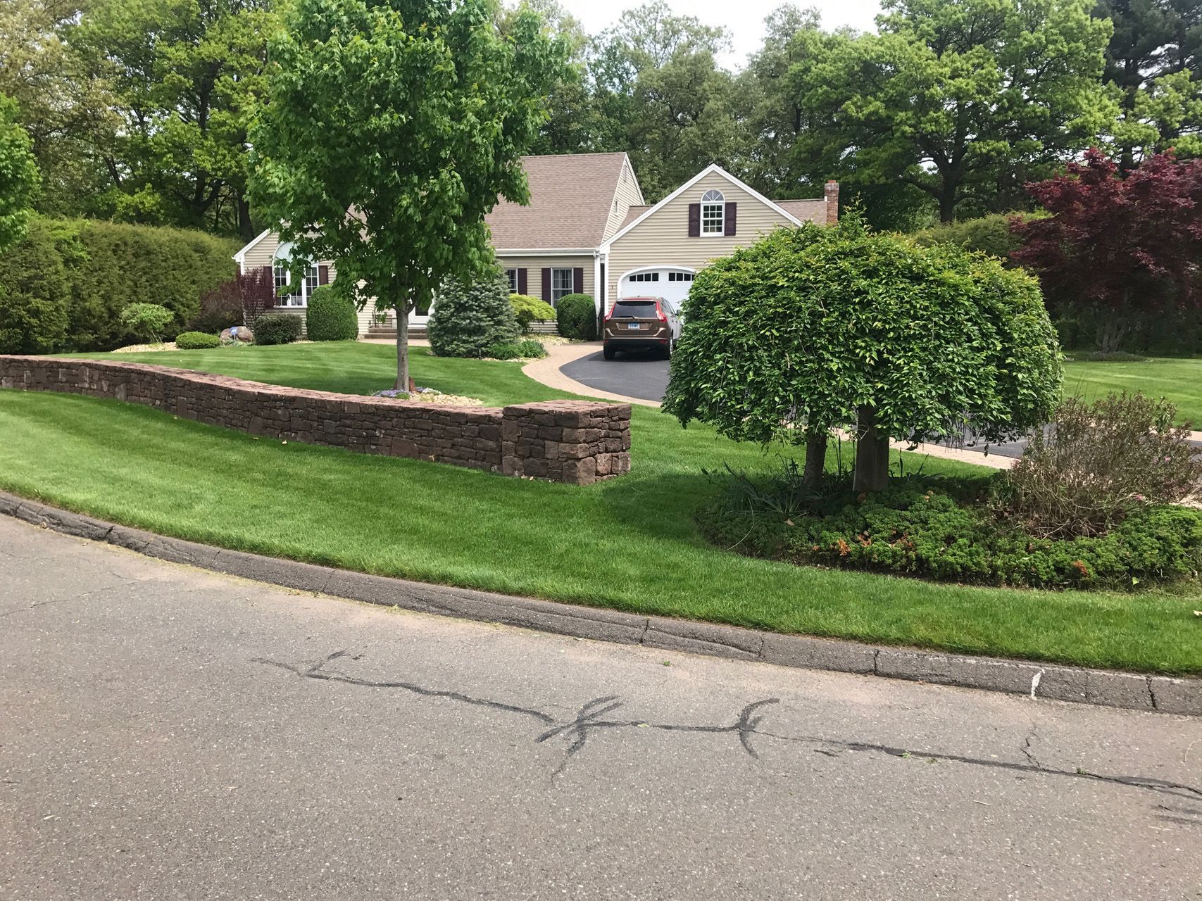 Suburban house with a driveway, parked car, and neatly landscaped front yard by the street