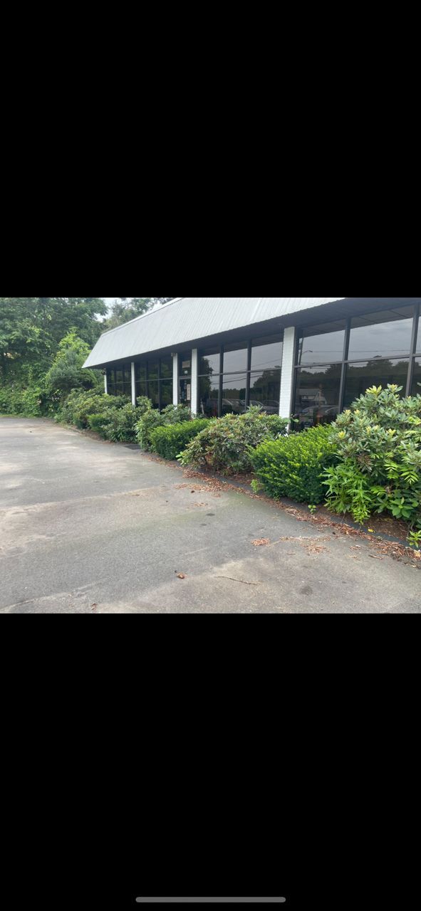 Covered roadside walkway beside a building, with bushes and a paved drive in the foreground.