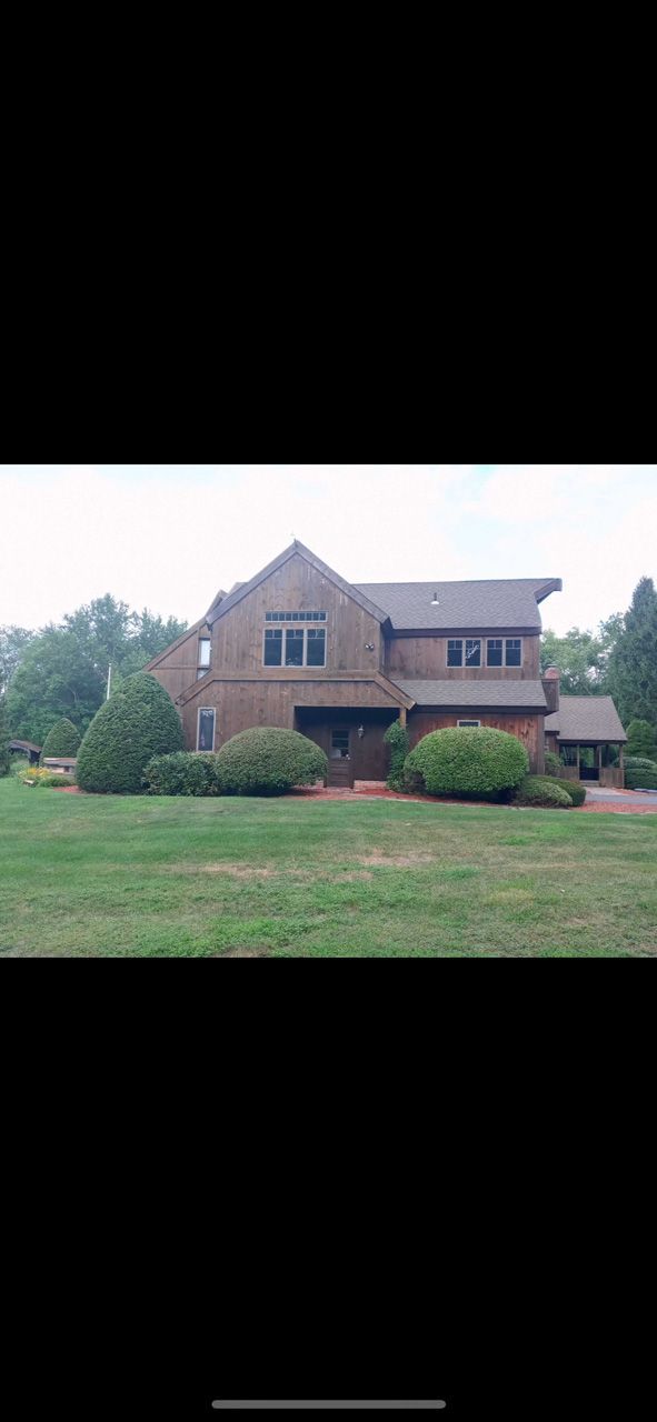 Brick house with a front lawn, shrubs, and a large gabled roof under an overcast sky