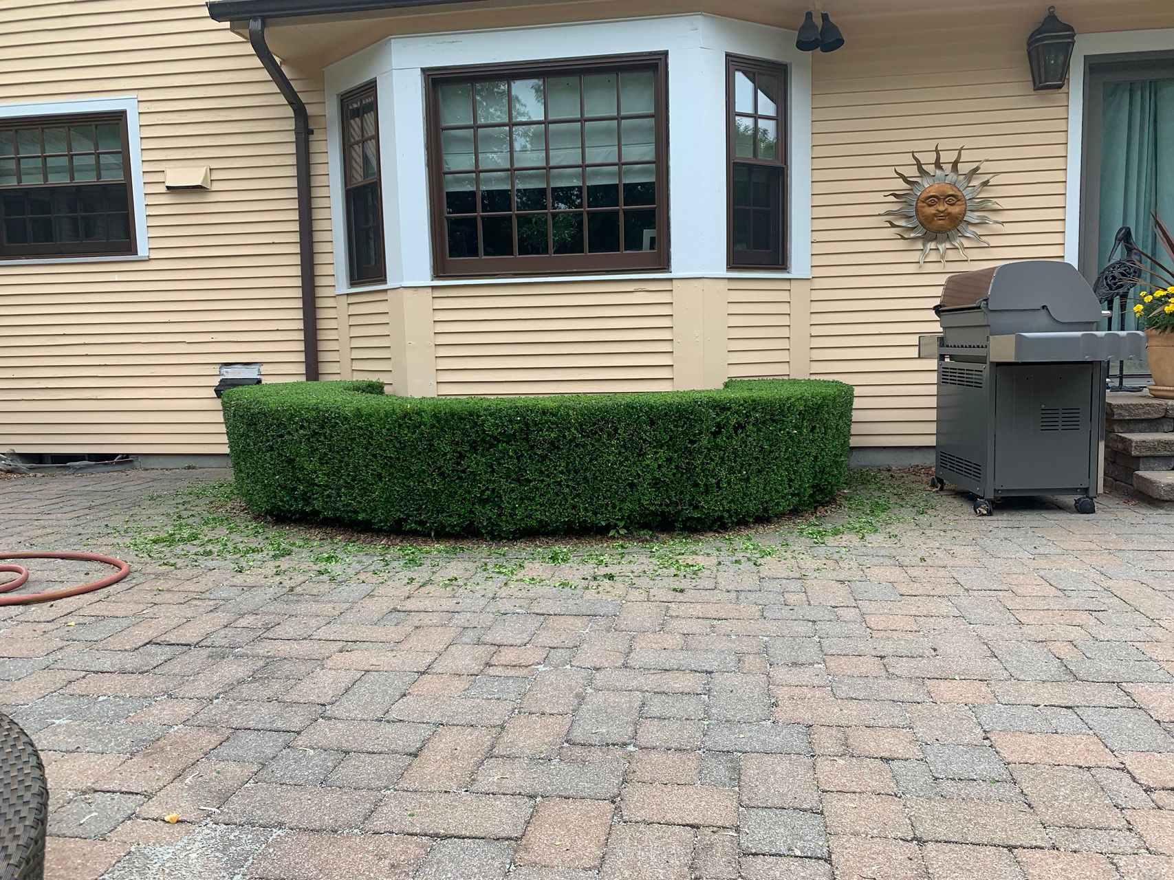 House exterior with a bay window, trimmed hedge, brick patio, and grill near the door