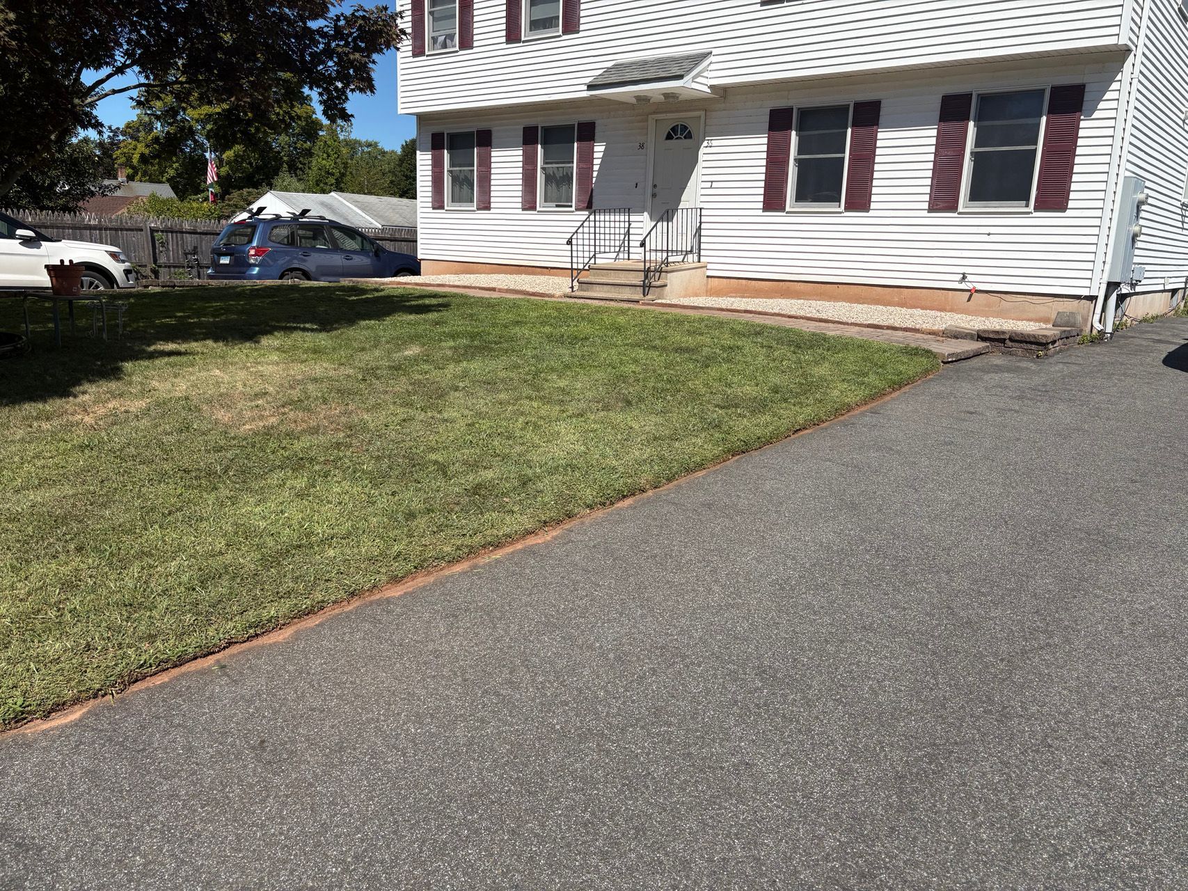 Suburban house with white siding, red shutters, front lawn, and driveway on a sunny day