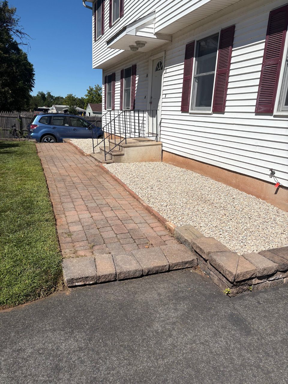 Brick walkway and steps leading to a house entrance with white siding and maroon shutters.
