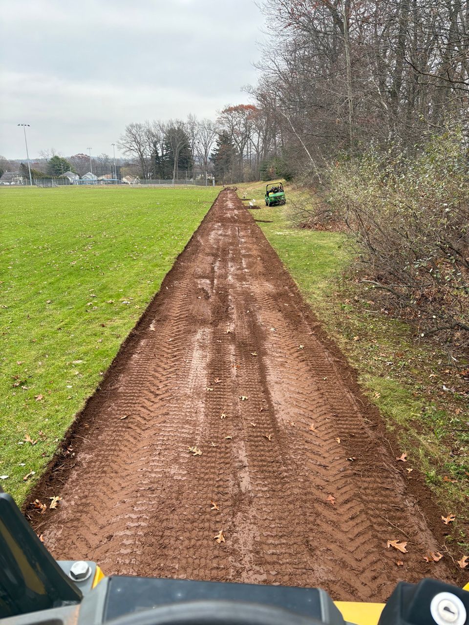 Dirt path through grassy field toward trees, with a small green tractor on the right.