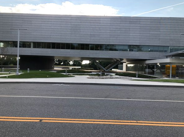 Modern gray building with a curved facade beside a road under a partly cloudy sky