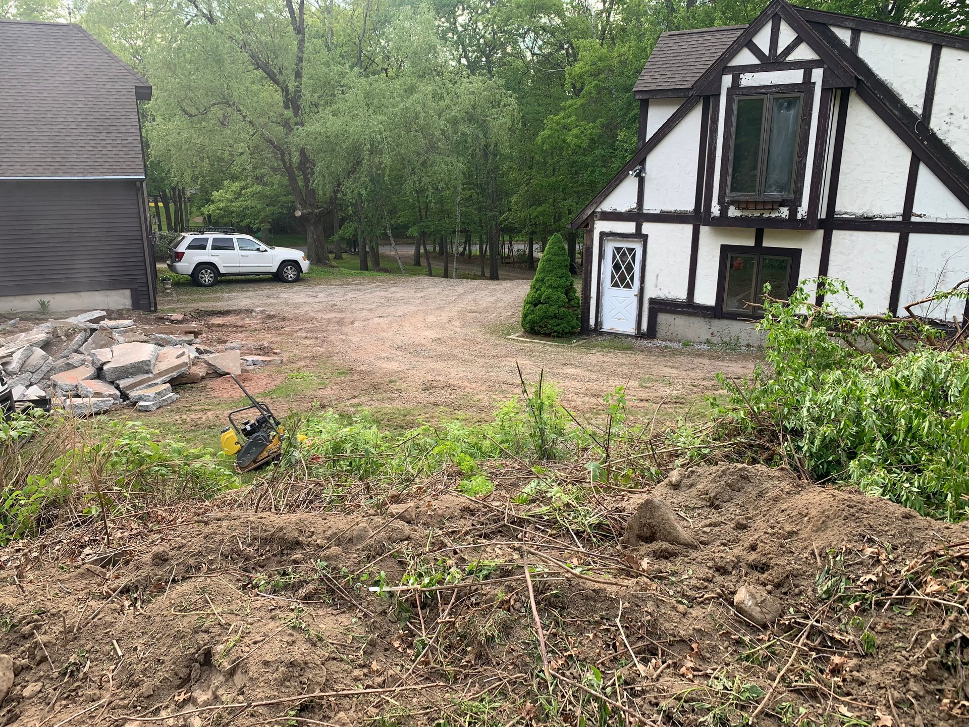 A cleared lot with a white SUV, a Tudor-style house, and a pile of debris in front.