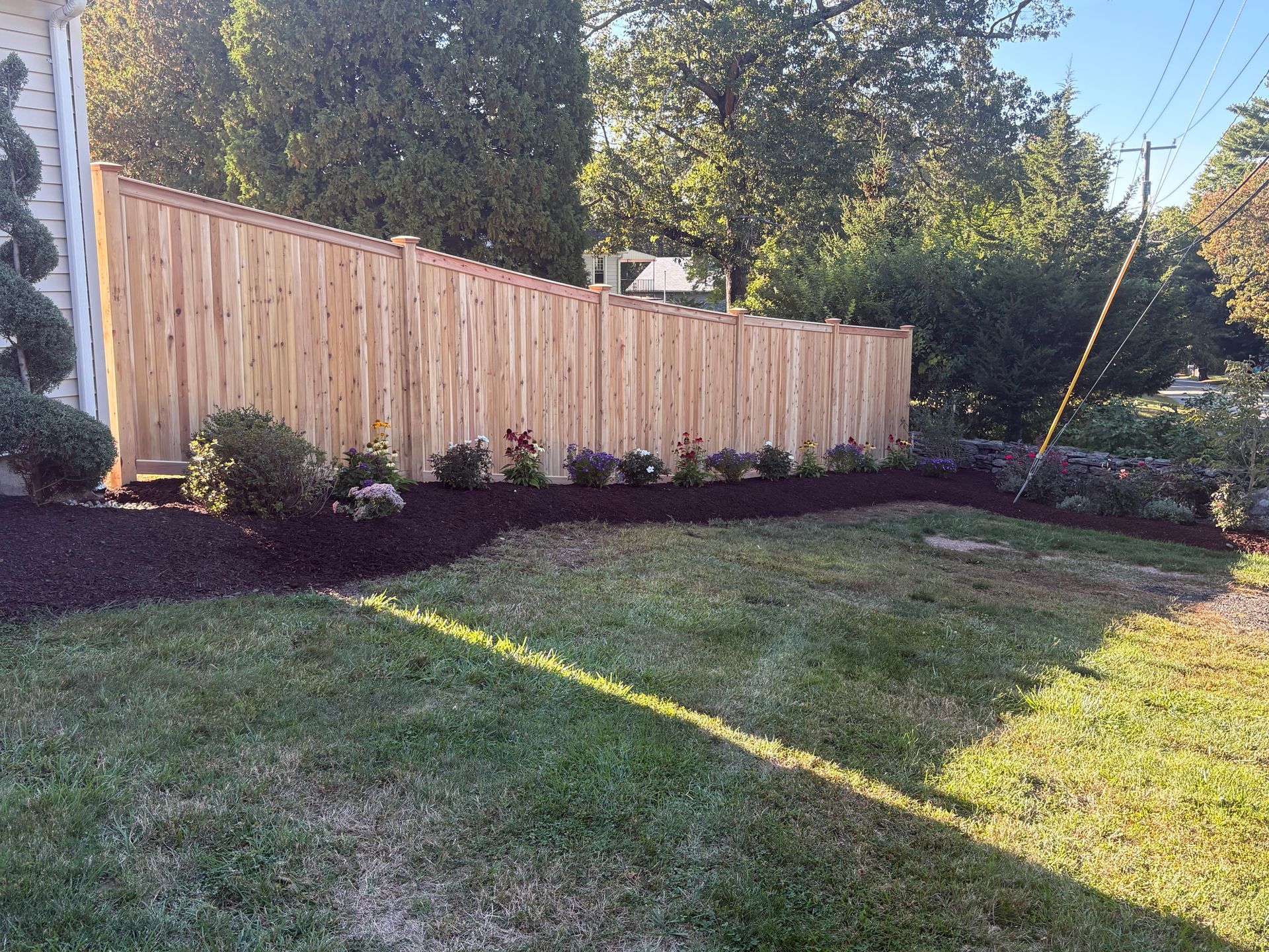 Wooden fence along a landscaped yard with green grass and dark mulch.