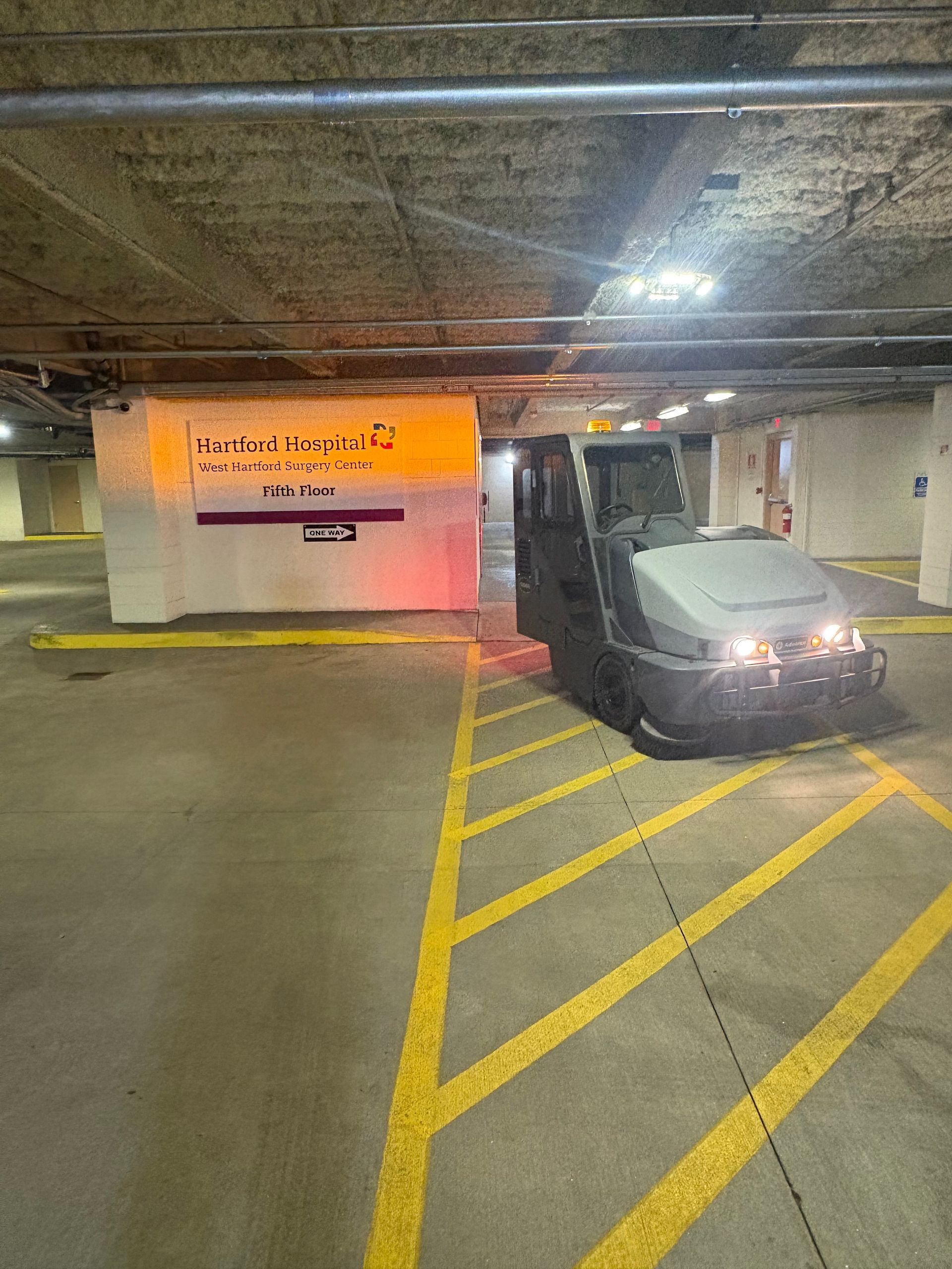 Car in an underground parking garage beside yellow hazard stripes and a wall sign.
