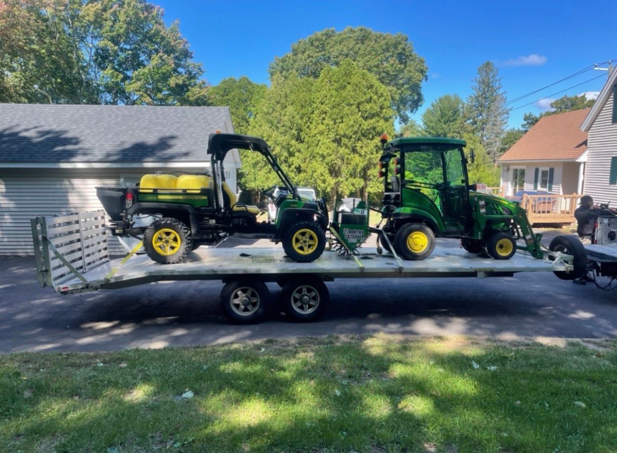 An orange Kubota excavator digging on a hillside, viewed from a white Bobcat vehicle. Forest backdrop.