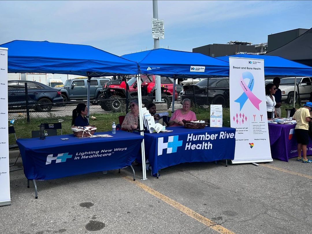 A group of people are sitting at tables under tents that say humber river health