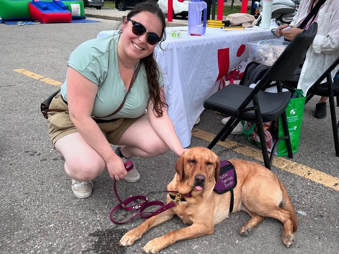 A woman is kneeling down next to a dog on a leash.