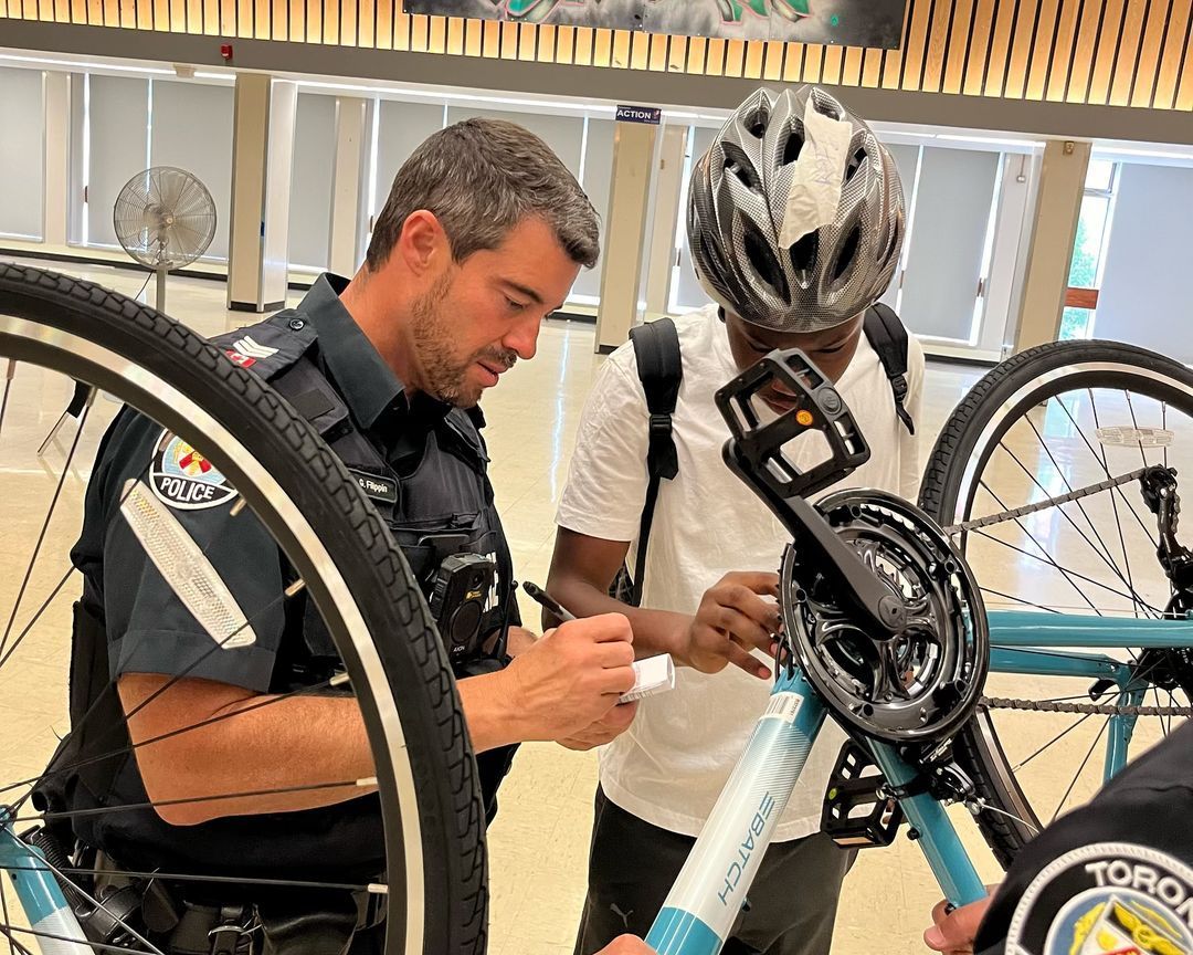 A police officer is talking to a man who is fixing a bicycle