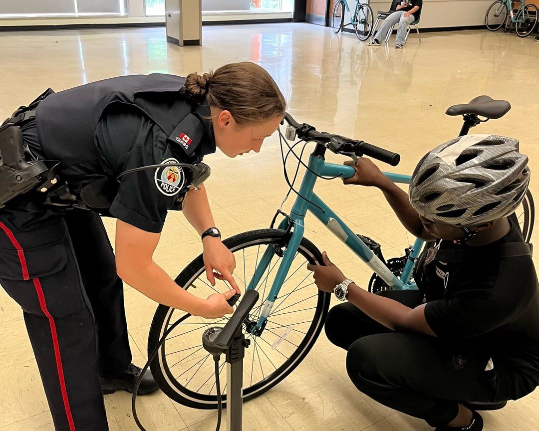 A police officer is helping another officer fix a bicycle