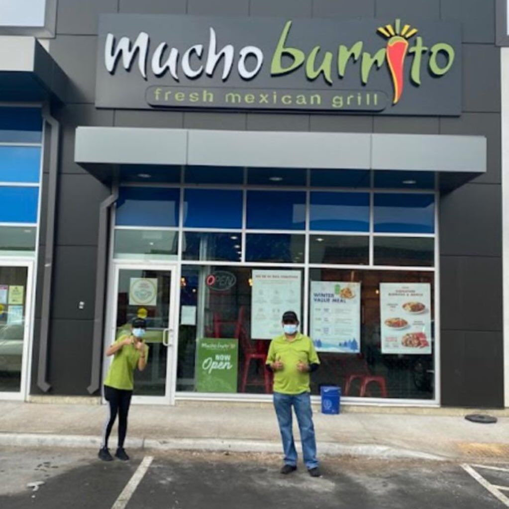two people wearing masks stand in front of a mucho burrito restaurant