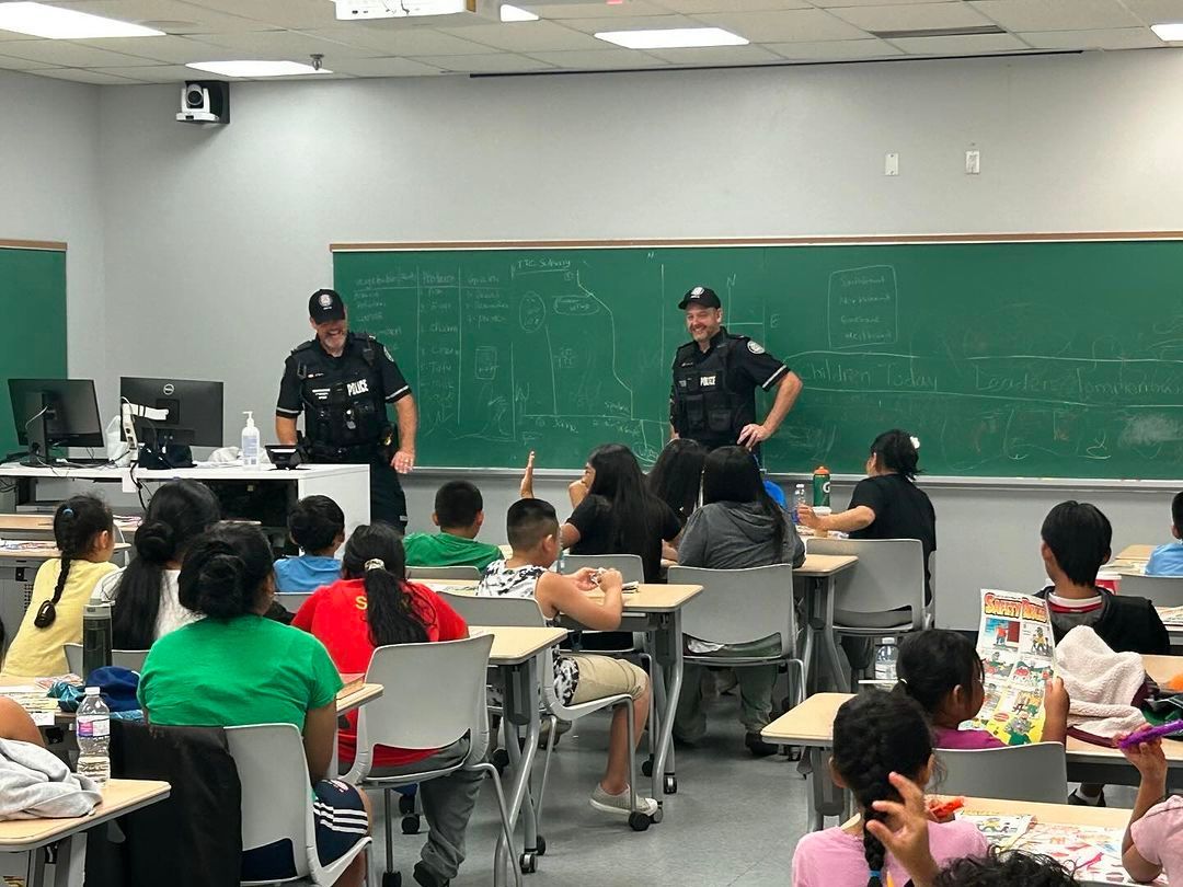 Two police officers are standing in front of a classroom full of children.