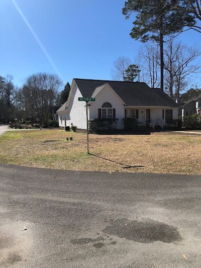 A white house with a black roof is sitting on top of a dirt field next to a road.