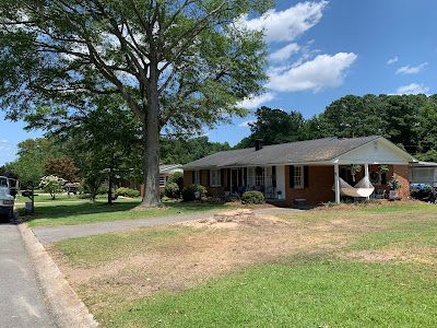A brick house with a porch and a tree in front of it.