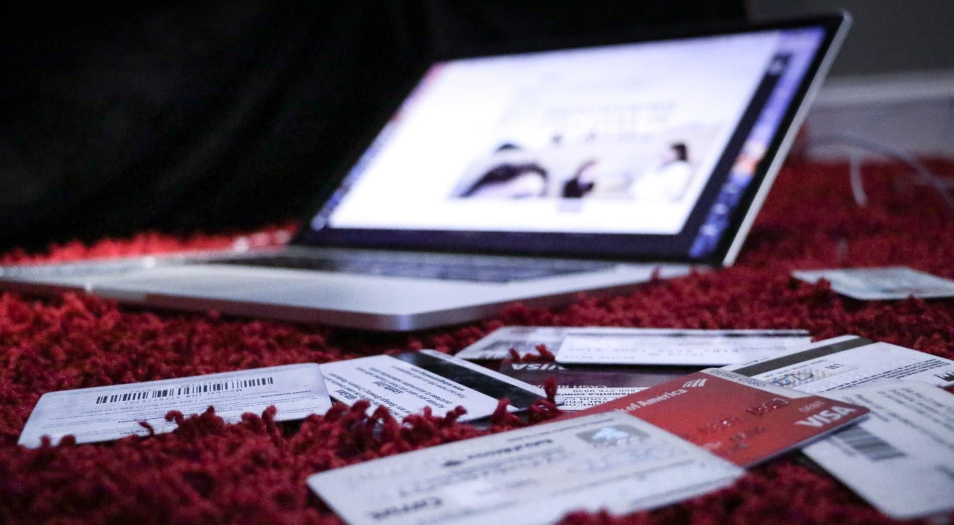 A laptop computer is sitting on a red rug next to credit cards.