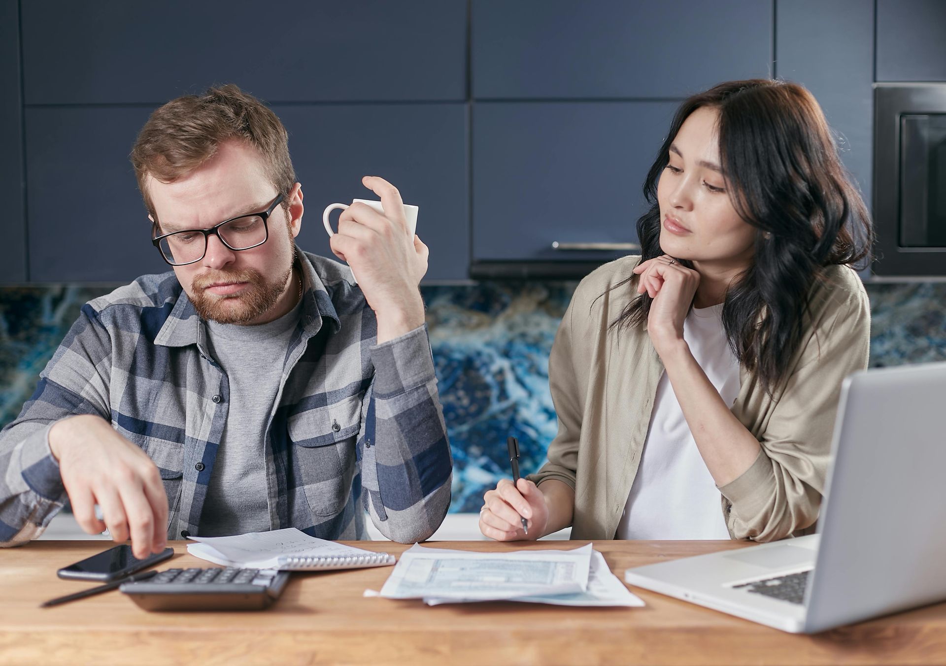 A man and a woman are sitting at a table with a laptop and a calculator.